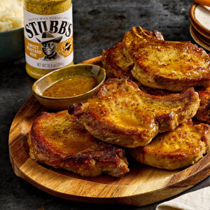A wooden platter features cooked pork chops with a side of Stubb's Moppin' Sauce.