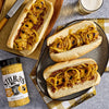 Three hot dogs topped with grilled onions and Stubb's Beef Spice Rub are displayed on a plate and wooden board.