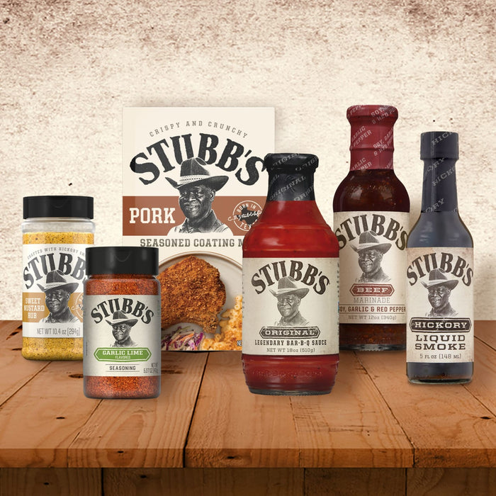 A collection of Stubb BBQ products including Stubbs Grlc Lime E seasoning and other sauces and rubs are displayed on a wooden table against a textured wall.