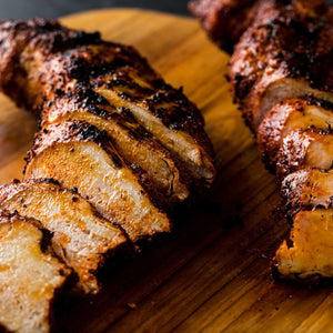 Slices of grilled pork tenderloin seasoned with Stubbs Grlc Lime E rest on a wooden cutting board.