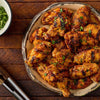 A platter of grilled chicken wings seasoned with Stubbs Grlc Lime E and garnished with fresh chopped herbs on a rustic wooden table.