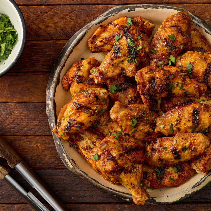 A platter of grilled chicken wings seasoned with Stubbs Grlc Lime E and garnished with fresh chopped herbs on a rustic wooden table.