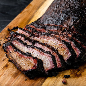 A wooden cutting board holds a perfectly sliced brisket prepared with Stubbs Smkhouse E featuring a dark bark and a prominent pink smoke ring.