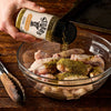 A person seasons a bowl of raw chicken wings with Stubbs Hkry Must E seasoning to prepare them for cooking.