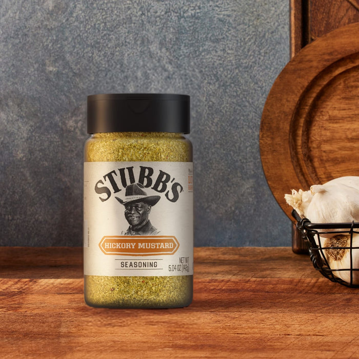 A bottle of Stubbs Hkry Must E seasoning sits on a rustic wooden surface next to a basket of fresh garlic.