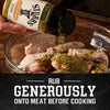 A person shakes a bottle of Stubbs Hkry Must E seasoning over a glass bowl of raw chicken wings to rub generously onto meat before cooking.