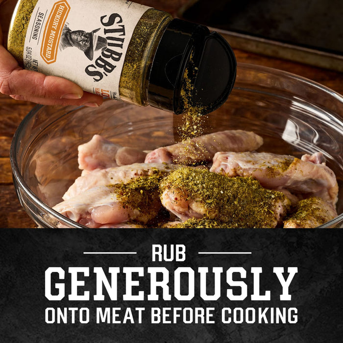 A person shakes a bottle of Stubbs Hkry Must E seasoning over a glass bowl of raw chicken wings to rub generously onto meat before cooking.