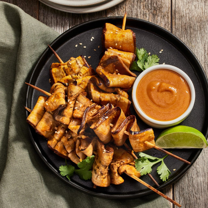 A plate of grilled eggplant skewers with a side of peanut sauce and lime.