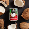 A can of Thai Kitchen coconut milk is surrounded by halved and whole coconuts.