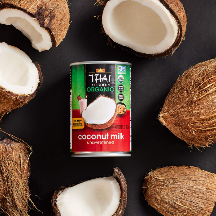A can of Thai Kitchen coconut milk is surrounded by halved and whole coconuts.