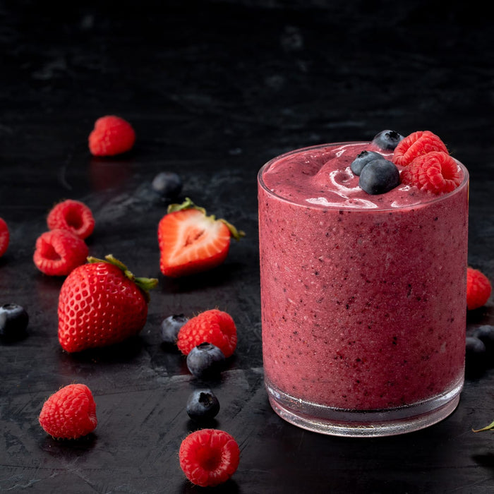 A vibrant berry smoothie is displayed in a glass, surrounded by fresh strawberries, raspberries, and blueberries on a dark surface.