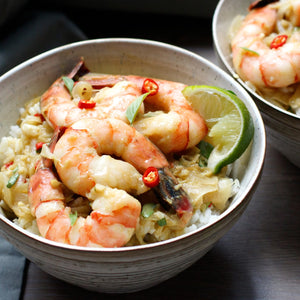 A bowl of shrimp with rice and a lime wedge.