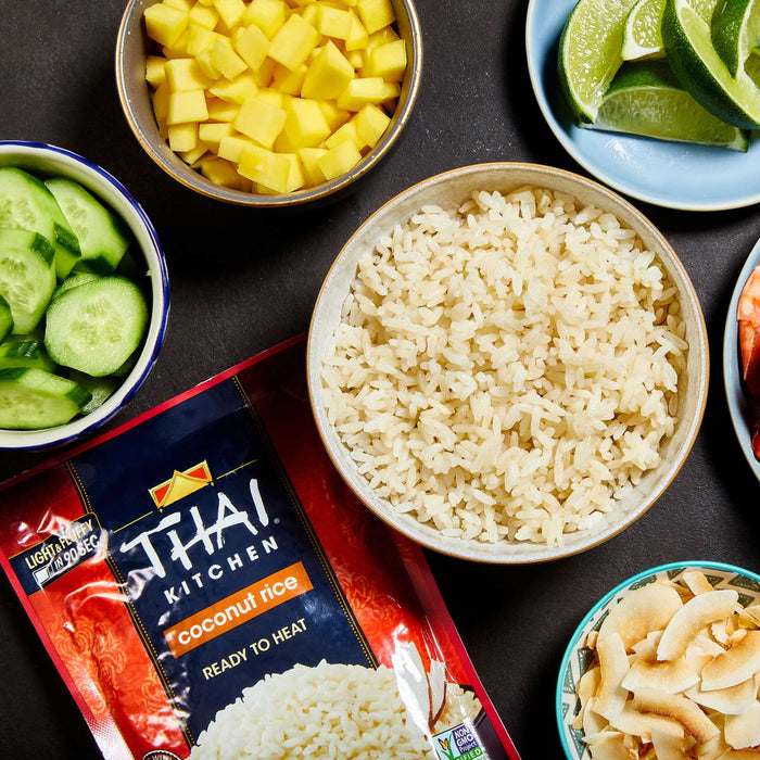 A bowl of Thai Kitchen coconut rice next to bowls of diced mango, cucumber slices, lime wedges, and coconut flakes.