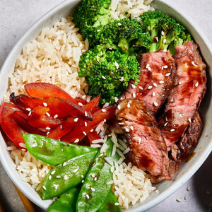A bowl of rice, broccoli, red peppers, snow peas, and steak.
