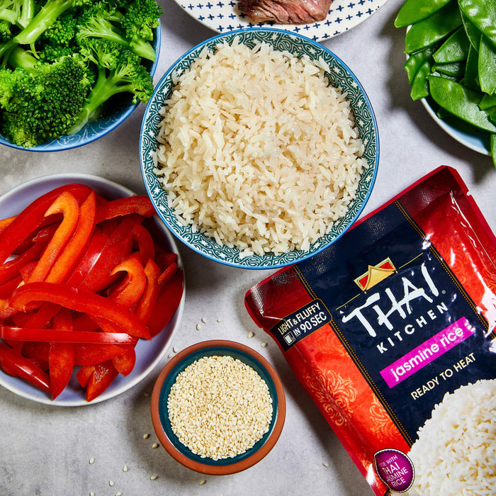A bowl of cooked Thai Kitchen jasmine rice with red bell peppers, broccoli, snow peas, and sesame seeds.
