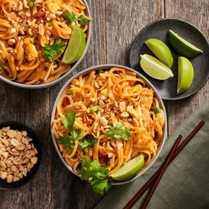 Two bowls of Pad Thai noodles with peanuts cilantro and lime wedges.