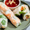 This is a close-up shot of fresh spring rolls with shrimp and vegetables served with a dipping sauce topped with peanuts.