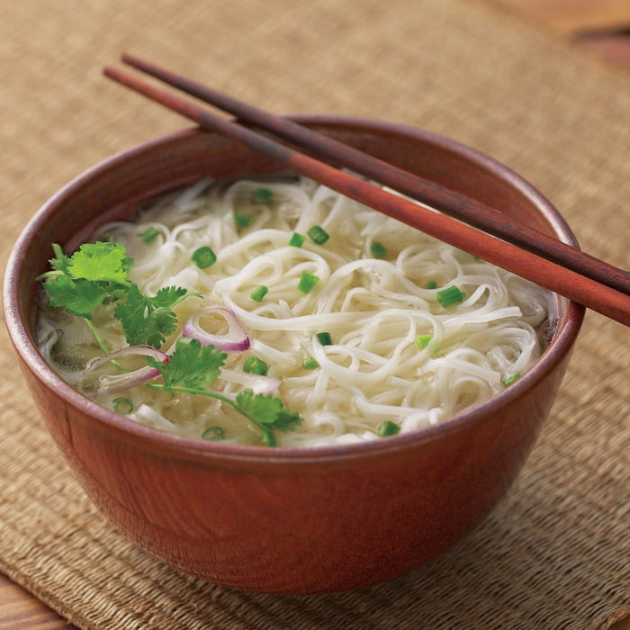 A bowl of noodle soup with chopsticks resting on top garnished with cilantro and green onions.
