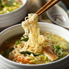 A bowl of noodle soup with asparagus and chicken is being eaten with chopsticks.