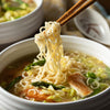 A bowl of noodle soup with asparagus and chicken is being eaten with chopsticks.