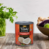 A can of Thai Kitchen coconut milk sits on a wooden surface, surrounded by fresh ingredients like ginger and herbs.
