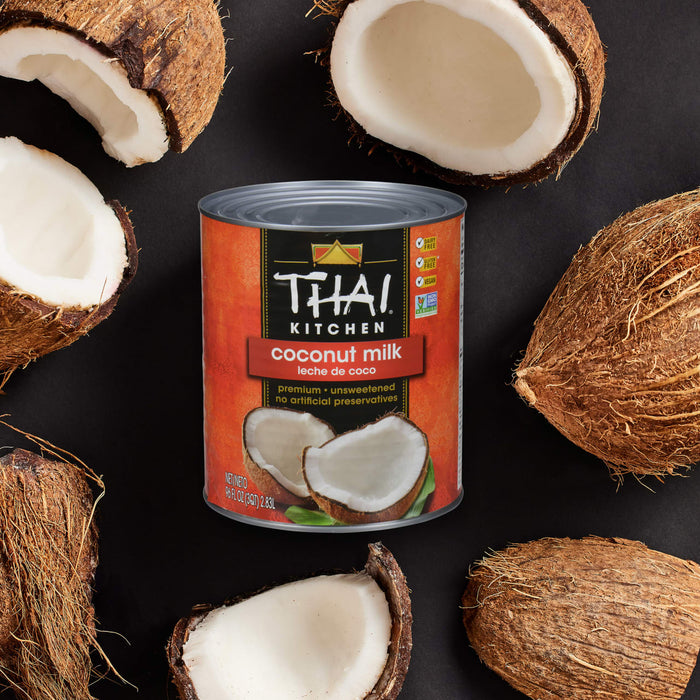A can of Thai Kitchen coconut milk is surrounded by fresh coconuts.