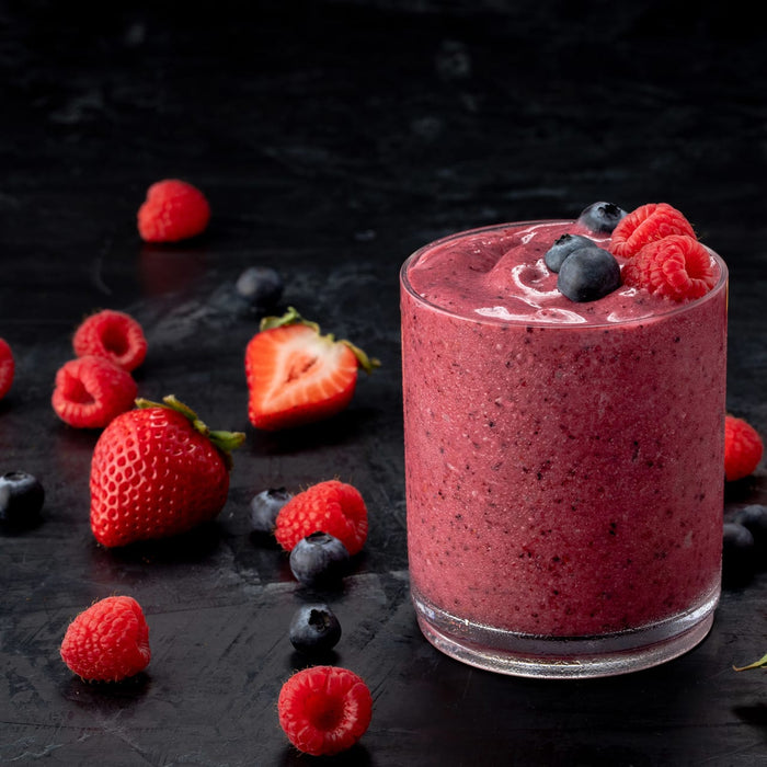A vibrant mixed berry smoothie is displayed in a glass, surrounded by fresh strawberries, raspberries, and blueberries.
