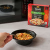 A prepared bowl of Thai Kitchen Chicken &amp; Rice with Thai Basil Sauce is ready to be eaten, with the red Thai Kitchen, 9.0 Oz product box and a microwave in the background.
