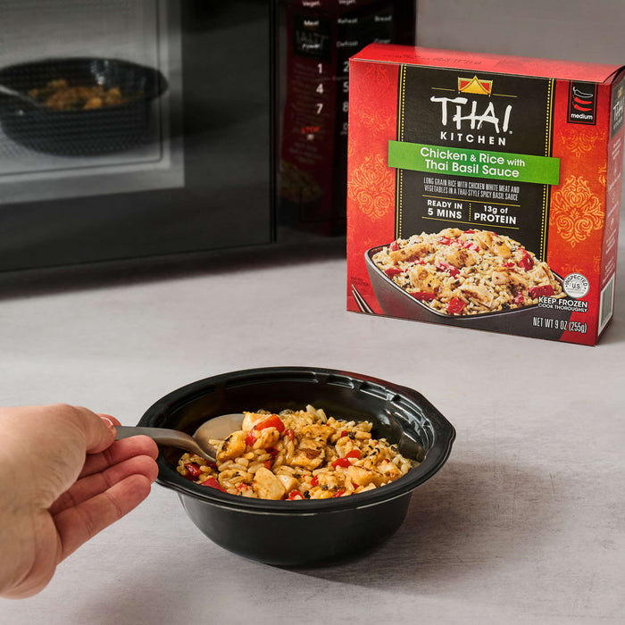 A prepared bowl of Thai Kitchen Chicken &amp; Rice with Thai Basil Sauce is ready to be eaten, with the red Thai Kitchen, 9.0 Oz product box and a microwave in the background.
