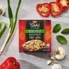 A box of Thai Kitchen, 9.0 Oz Chicken &amp; Rice with Thai Basil Sauce is displayed on a gray surface, surrounded by fresh ingredients like red bell peppers, garlic, scallions, and basil leaves.