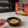 A person eats a prepared bowl of a Thai Kitchen, 9.0 Oz meal of Coconut Red Curry Sauce with Chicken &amp; Rice, with the product box shown next to a microwave.