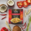 A box of Thai Kitchen, 9.0 Oz Coconut Red Curry Sauce with Chicken &amp; Rice is displayed on a gray surface surrounded by fresh ingredients like coconut, red chili peppers, and lemongrass.