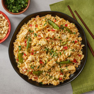 A black bowl filled with a finished recipe of chicken and rice made with Thai Kitchen, 9.0 Oz, is shown with side bowls of peanuts and cilantro.