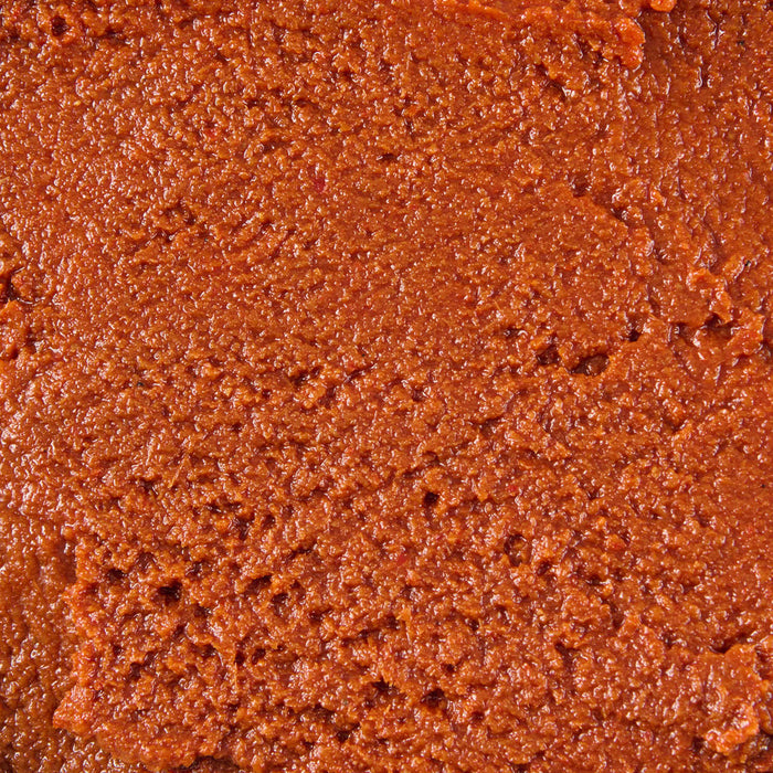 A close-up, top-down view reveals the rich, reddish-orange color and coarse, moist texture of Thai Kitchen Red Curry Paste.