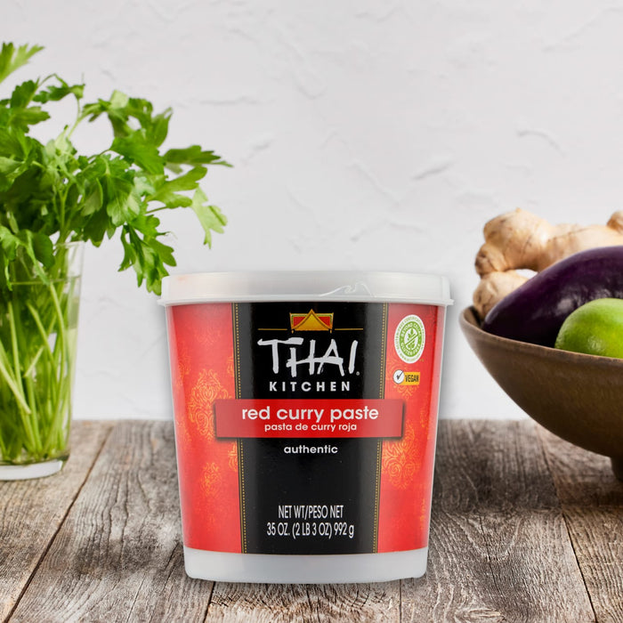 A container of Thai Kitchen Red Curry Paste sits on a wooden surface, suggesting its use in preparing authentic Thai cuisine.