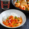 A bowl of rice and Thai red curry shrimp with a container of Thai Kitchen red curry paste in the background.