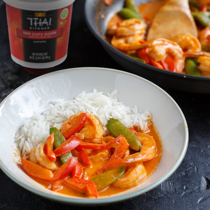 A bowl of rice and Thai red curry shrimp with a container of Thai Kitchen red curry paste in the background.