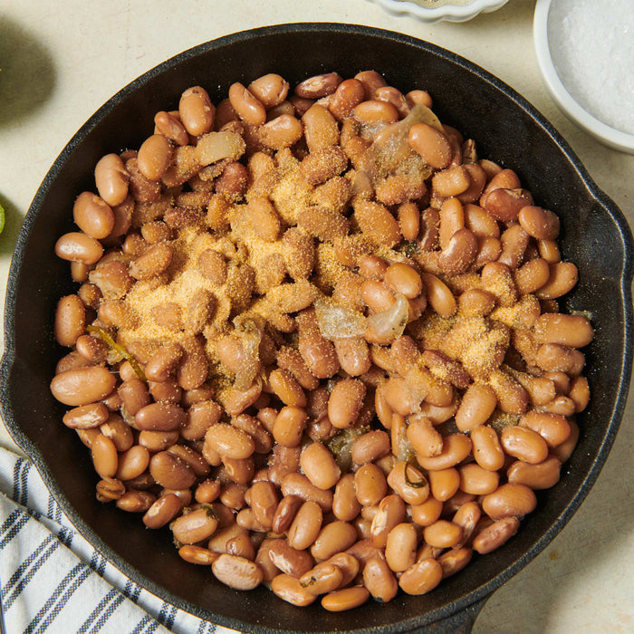 A skillet filled with cooked pinto beans and onions, likely part of a Southwestern or Tex-Mex meal.