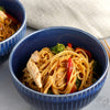 A blue bowl filled with noodles, chicken, broccoli, and red peppers.