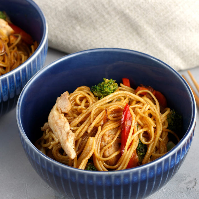 A blue bowl filled with noodles, chicken, broccoli, and red peppers.