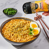 A bowl of ramen is being sprinkled with Tajin seasoning, garnished with a halved boiled egg and chopped greens.
