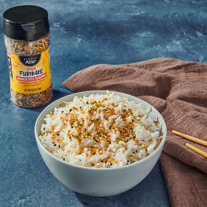 A bowl of rice sprinkled with Trader Joe's Furikake Japanese Multi-Purpose Seasoning is displayed next to the seasoning container.