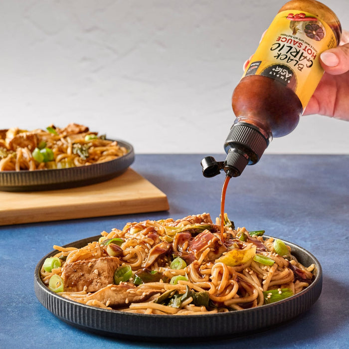 A person is pouring Bachan's Japanese Barbecue Sauce onto a plate of noodles with meat and vegetables.