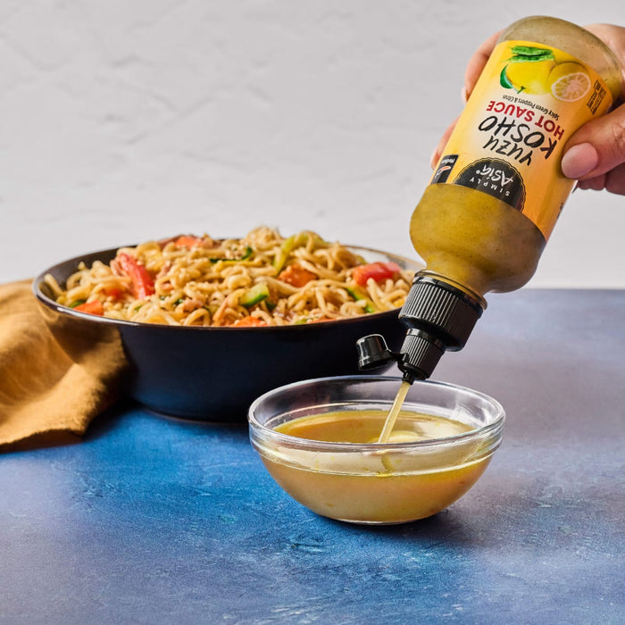 A bottle of Kevin's Teriyaki Sauce is being poured into a bowl, with a pan of noodles in the background.