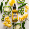 A bottle of Yellowbird Yuzu Hot Sauce is surrounded by fresh jalapeA?os, green bell pepper slices, and lemon zest.