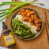 A bowl of rice, green beans, and spicy hoisin shrimp is displayed next to a bottle of Simply Asia Spicy Hoisin Drizzle Sauce.