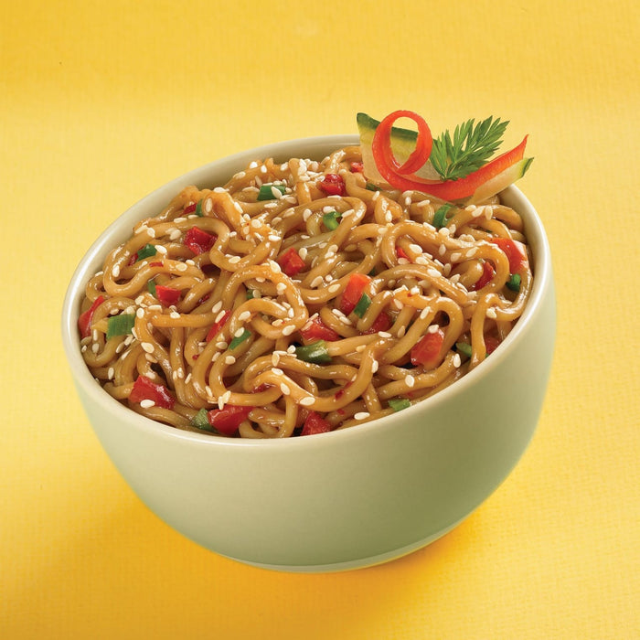 A bowl of noodles with sesame seeds, red peppers, and green onions.