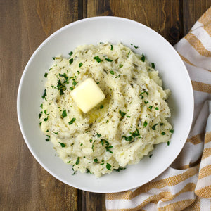 A bowl of mashed potatoes with parsley and a pat of butter next to a tube of Gourmet Garden Parsley Stir-In Paste.