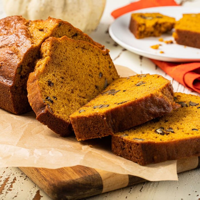 Slices of pumpkin bread with nuts on a wooden cutting board.