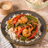 A plate of shrimp stir fry with rice, red peppers, and snow peas.